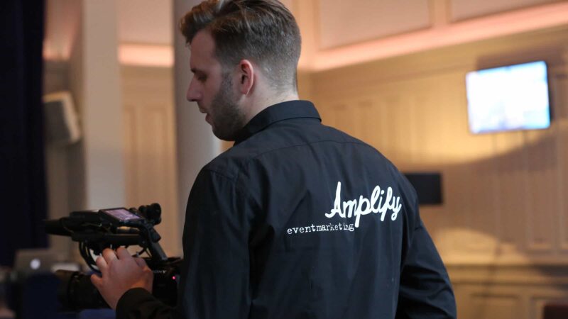 Cameraman op een event met een zwarte blouse met Amplify Eventmarketing erop