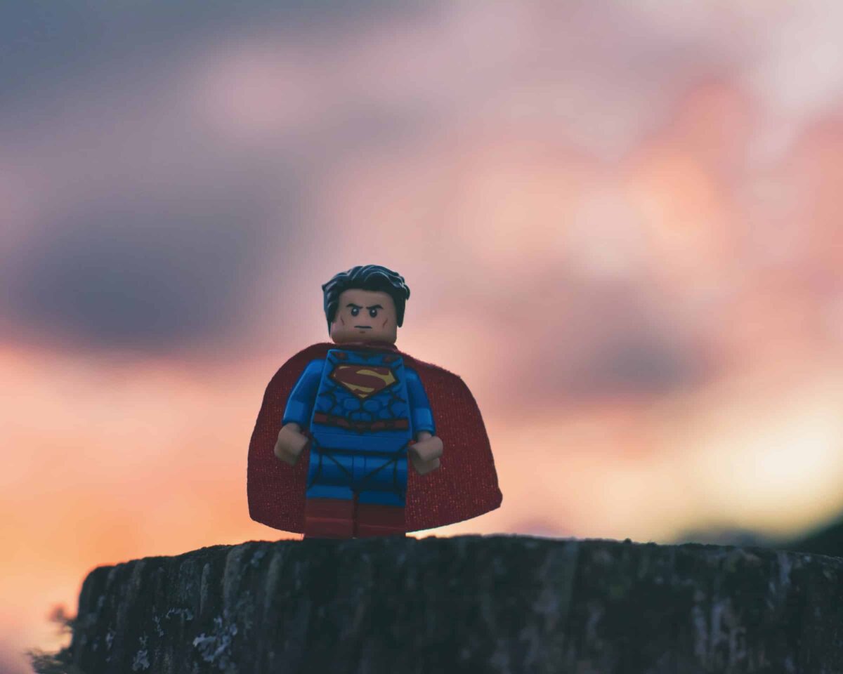 Superman legopoppetje op een boomstronk bij zonsondergang (Photo@esteban-lopez)