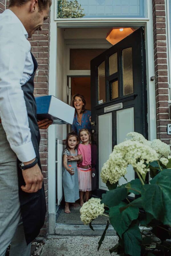 Vrouw met twee kinderen die de deur open doen als er een pakket wordt bezorgd