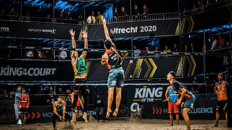 Twee beachvolleyballers die omhoog springen bij het net tijdens King of the Court (foto-SetVexy)