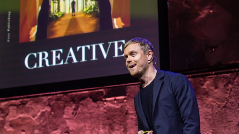 Timo foto van spreker tijdens congres met een presentatie op achtergrond en het woord creative