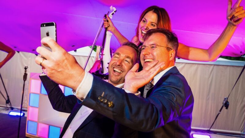 Twee mannen die op de foto gaan met een violist tijdens een feest in een tent - Photo: Tycho's Eye Photography