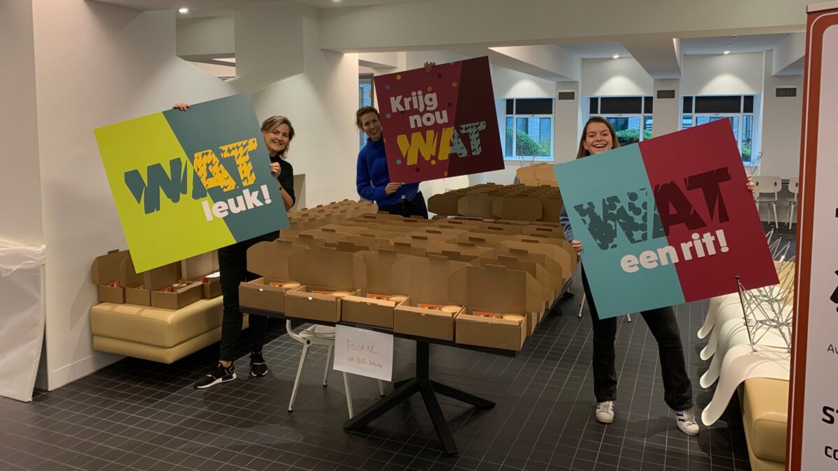 Ingepakte pakketten met 3 medewerkers met borden met teksten wat leuk, krijg nou wat en wat een rit