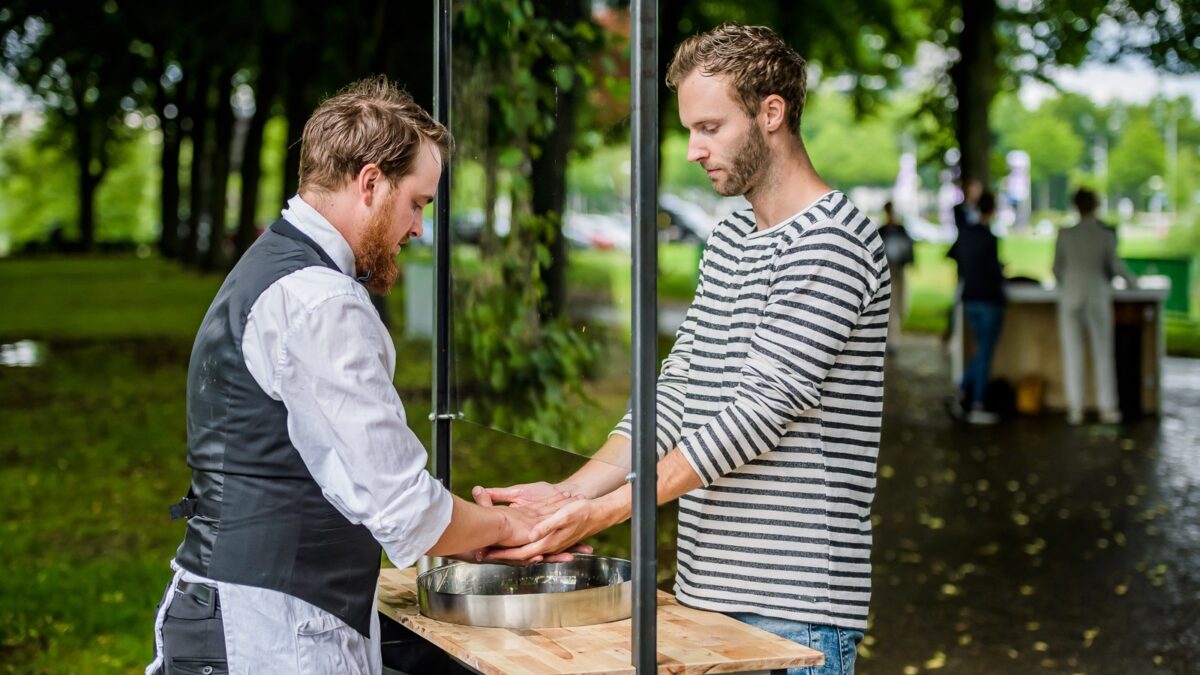 De wasmannen - handen wassen achter een scherm